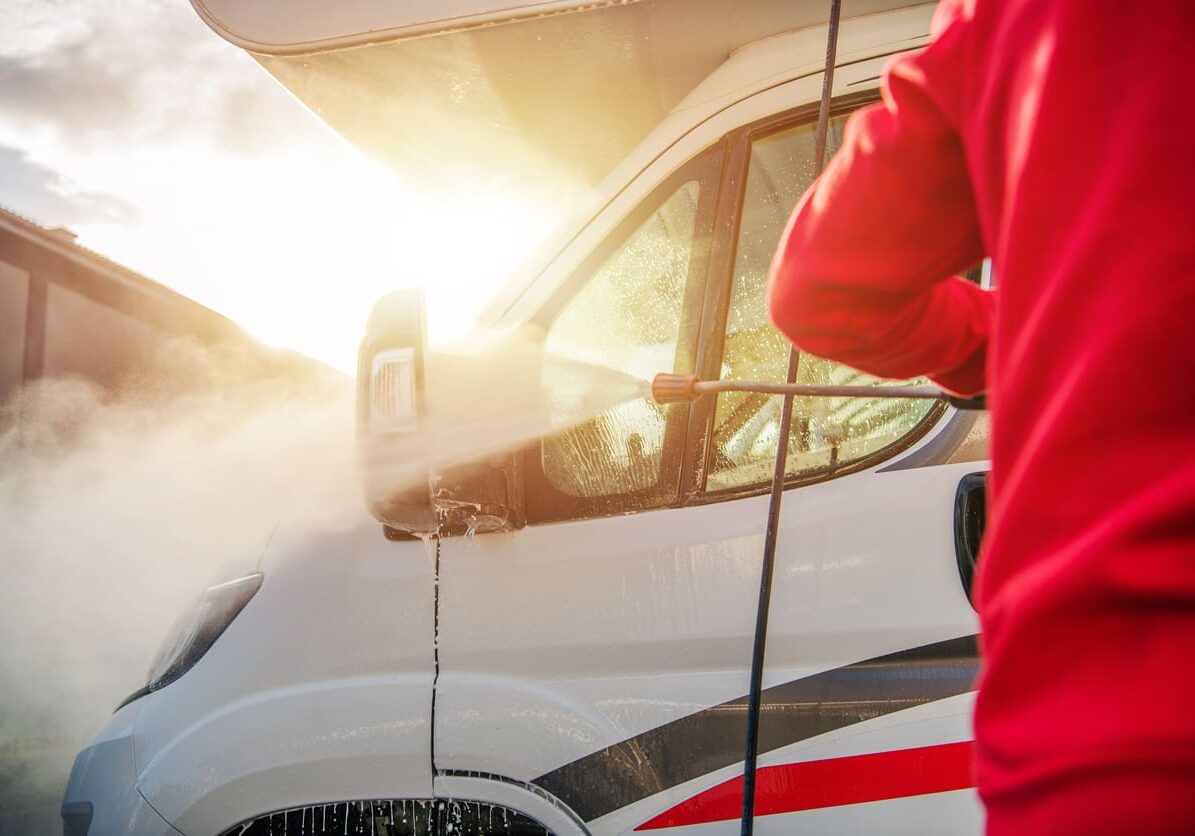 A person in red overalls is spraying water on a white van.